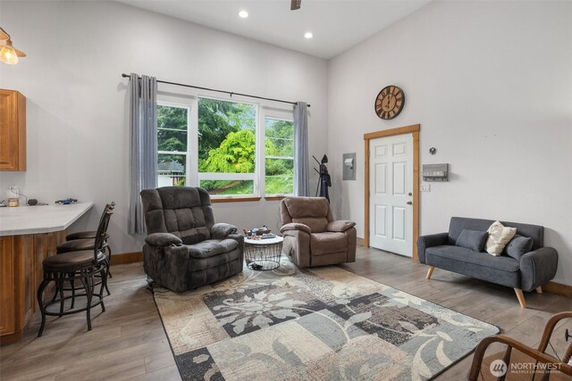 living room with wood-type flooring, recessed lighting, baseboards, ceiling fan, and a towering ceiling