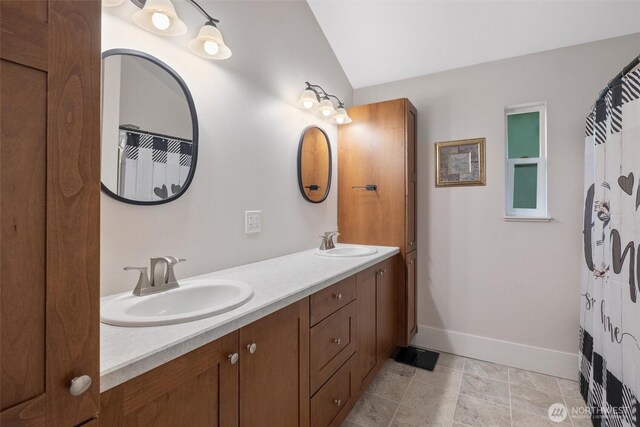 full bathroom with baseboards, vaulted ceiling, and double vanity