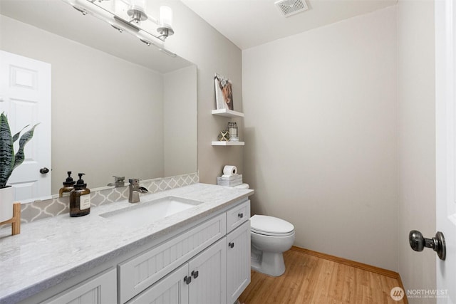 half bathroom with vanity, wood finished floors, toilet, and baseboards