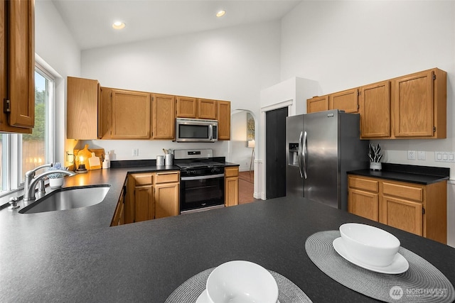 7725 Perregrine Pl, Arlington, WA 98223 - kitchen with stainless steel appliances, a sink, high vaulted ceiling, dark countertops, and brown cabinets