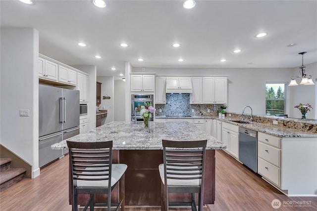 kitchen featuring stainless steel appliances, a sink, a peninsula, wood finished floors, and recessed lighting