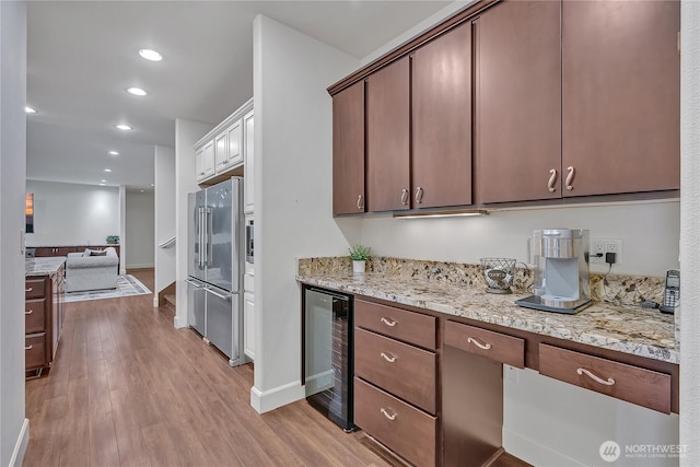kitchen featuring beverage cooler, high end refrigerator, light wood-style flooring, light stone counters, and recessed lighting