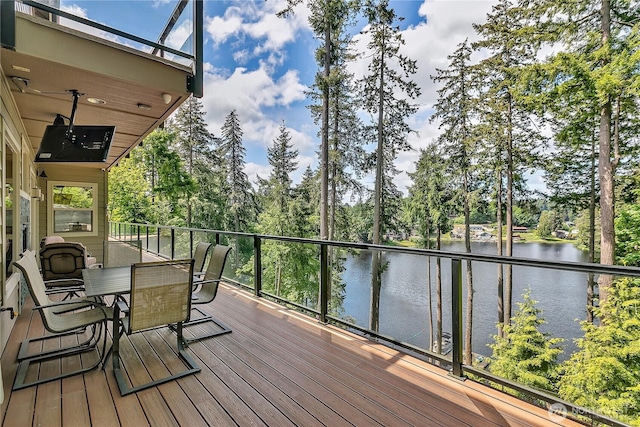 deck with a water view, view of wooded area, and outdoor dining area