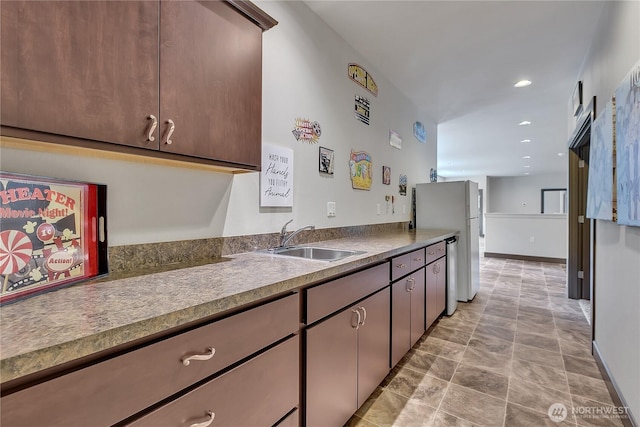 kitchen with a sink, freestanding refrigerator, stone finish flooring, recessed lighting, and stainless steel dishwasher