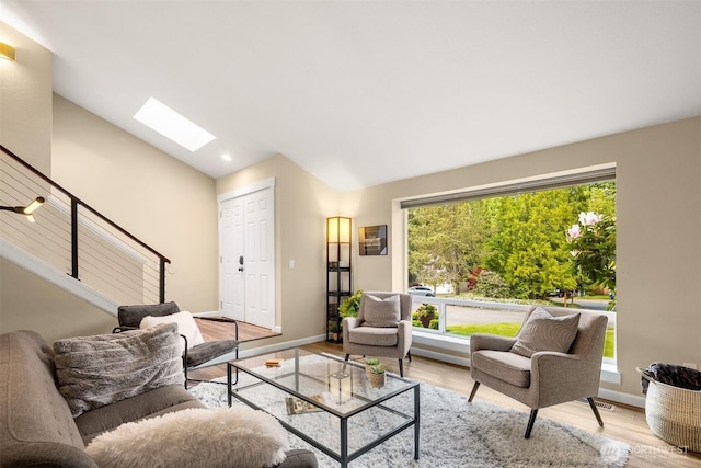 living area featuring vaulted ceiling, a skylight, wood finished floors, healthy amount of natural light, and baseboards