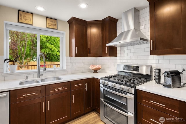 kitchen with appliances with stainless steel finishes, a sink, wall chimney exhaust hood, light countertops, and recessed lighting