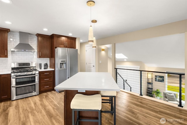 kitchen with wall chimney exhaust hood, stainless steel appliances, light wood-style flooring, light countertops, and tasteful backsplash