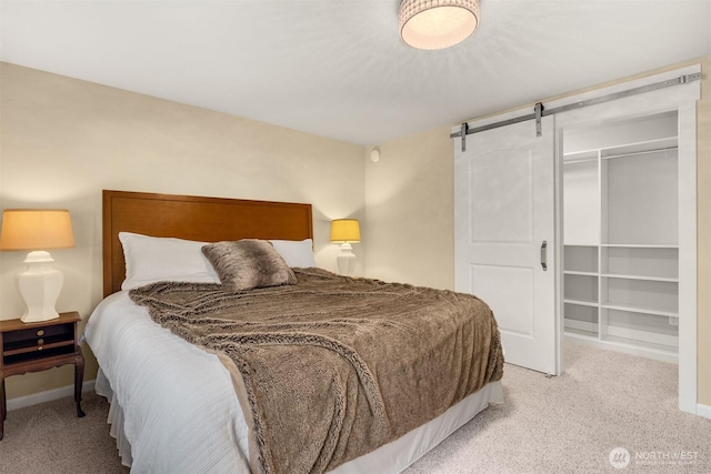 bedroom with light carpet, a barn door, baseboards, and a closet
