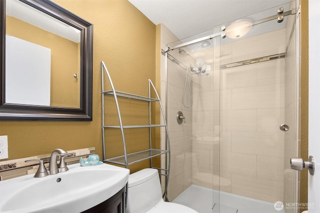 bathroom featuring toilet, a stall shower, a textured wall, and vanity
