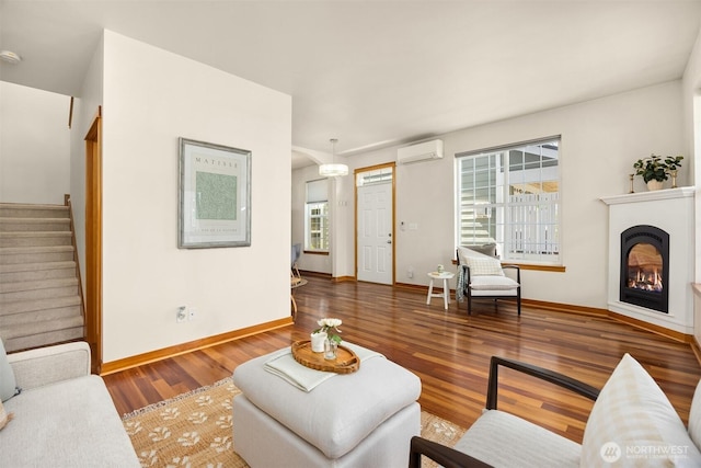 living area featuring a wall mounted air conditioner, wood finished floors, stairway, baseboards, and a glass covered fireplace