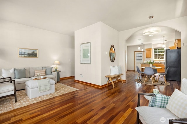 living area featuring arched walkways, wood finished floors, and baseboards