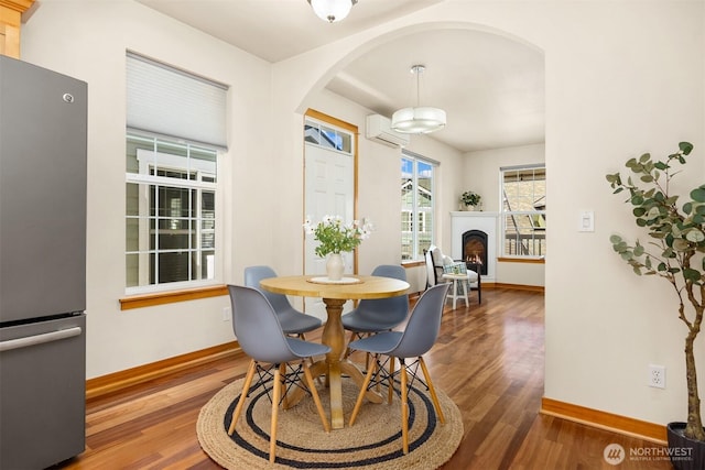 dining space with arched walkways, baseboards, and wood finished floors