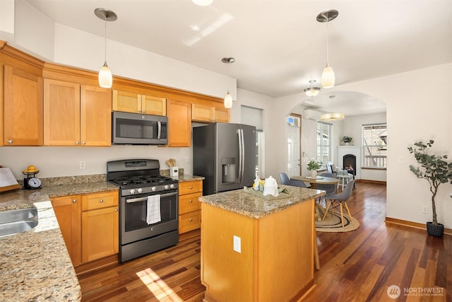 kitchen featuring appliances with stainless steel finishes, arched walkways, dark wood-type flooring, and a kitchen island