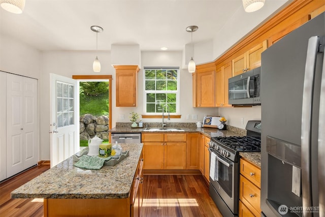 kitchen with appliances with stainless steel finishes, a sink, dark wood-style floors, stone countertops, and a center island
