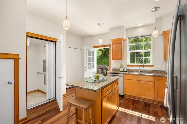 kitchen with a sink, appliances with stainless steel finishes, dark wood-style flooring, light stone countertops, and a kitchen island