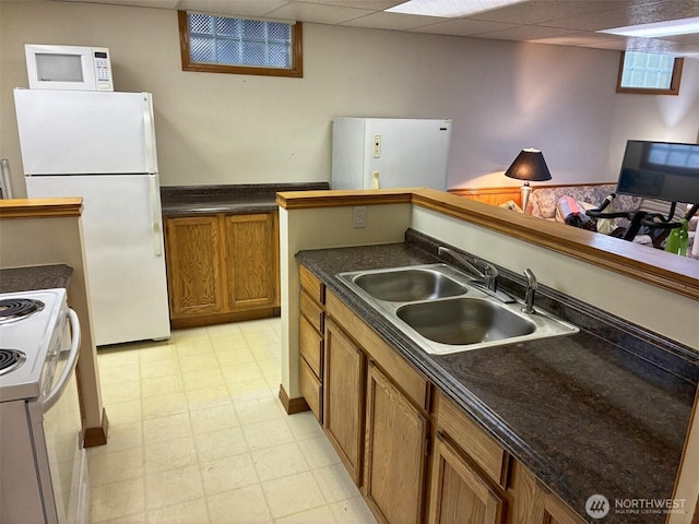 kitchen with white appliances, a sink, light floors, dark countertops, and brown cabinetry
