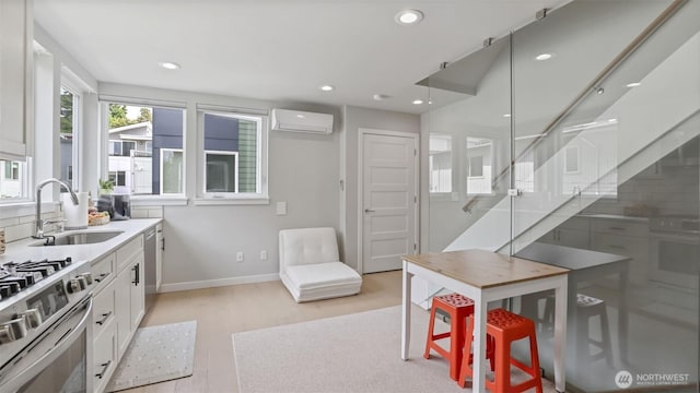 kitchen with a wall unit AC, a sink, stainless steel appliances, light wood-style floors, and white cabinetry