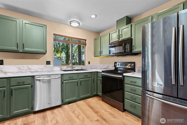 kitchen with appliances with stainless steel finishes, green cabinetry, a sink, and light wood-style floors