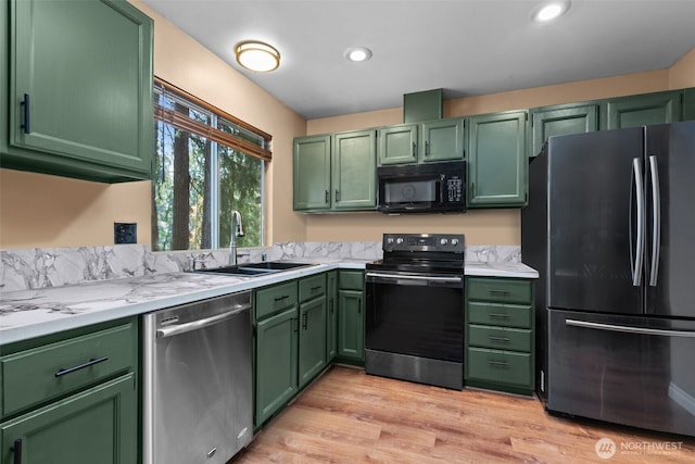 kitchen featuring black appliances, green cabinets, a sink, light countertops, and light wood-style floors