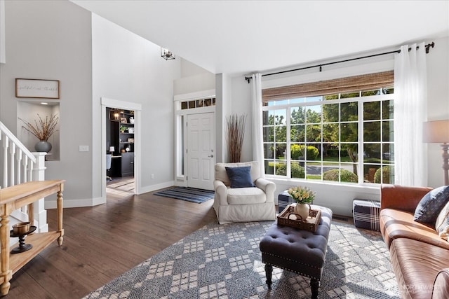 living room featuring stairs, wood finished floors, baseboards, and a towering ceiling