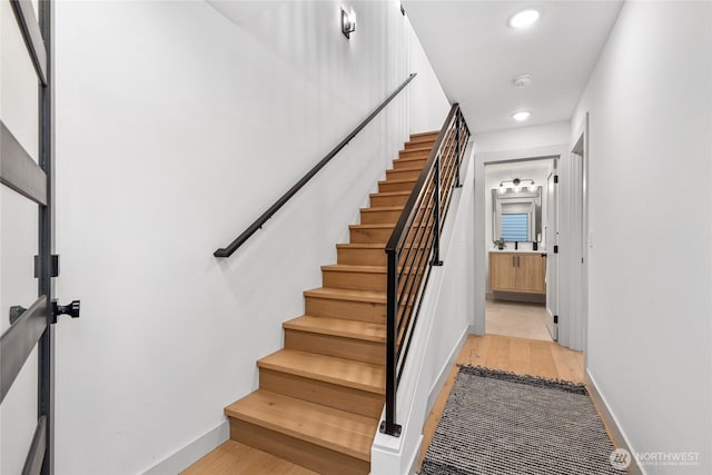 staircase with wood finished floors, baseboards, and recessed lighting