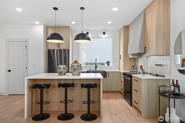 kitchen featuring freestanding refrigerator, black electric range oven, light brown cabinetry, a sink, and light wood finished floors