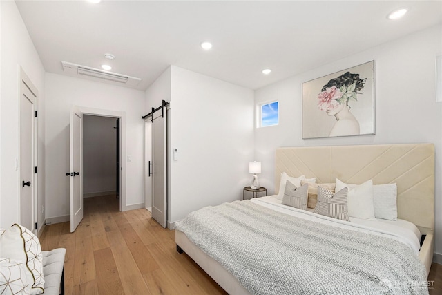 bedroom with a barn door, light wood-type flooring, baseboards, and recessed lighting