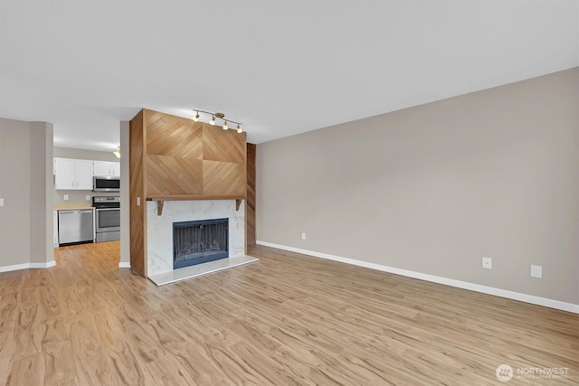1175 Harrington Pl NE Unit 101, Renton, WA 98056 - unfurnished living room with track lighting, light wood-style flooring, baseboards, and a premium fireplace