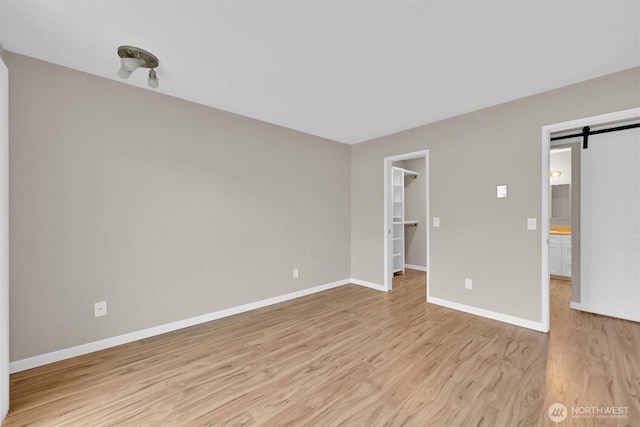 1175 Harrington Pl NE Unit 101, Renton, WA 98056 - unfurnished bedroom featuring a barn door, light wood-style floors, baseboards, a walk in closet, and a closet