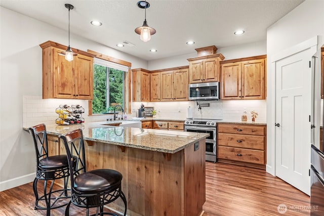 kitchen featuring stainless steel appliances, a sink, light stone countertops, a breakfast bar area, and wood finished floors