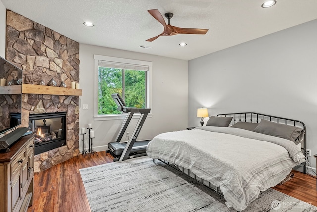 bedroom with wood finished floors, a stone fireplace, ceiling fan, recessed lighting, and baseboards