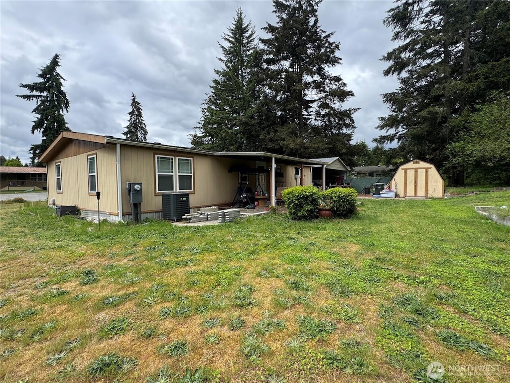 rear view of property with a storage unit, a lawn, central air condition unit, an outdoor structure, and a patio