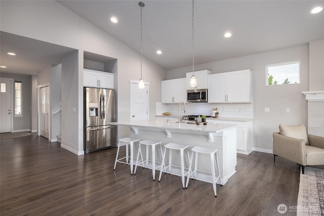 kitchen featuring stainless steel appliances, decorative backsplash, a breakfast bar area, dark wood-type flooring, and white cabinetry