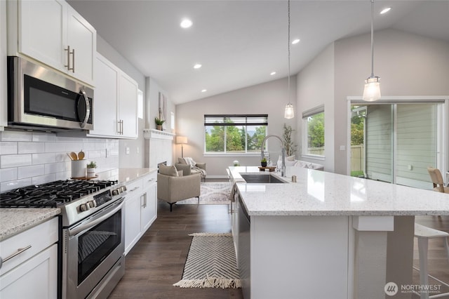 kitchen featuring stainless steel appliances, lofted ceiling, a sink, backsplash, and open floor plan