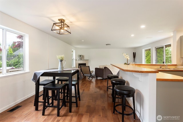 dining space featuring a fireplace, wood finished floors, recessed lighting, baseboards, and bar with sink