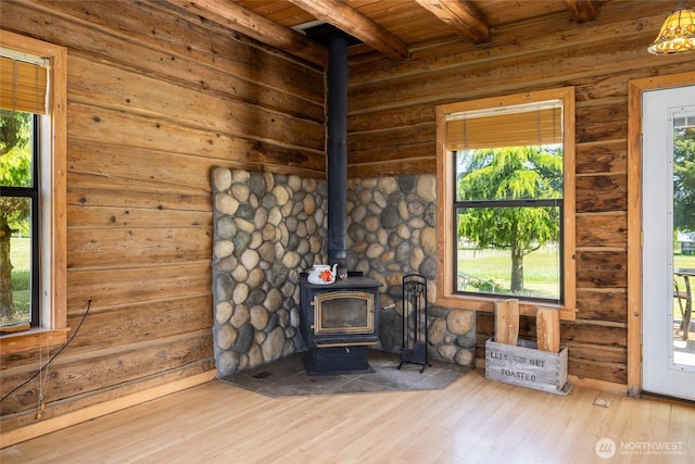 unfurnished living room with a wood stove, beamed ceiling, wood ceiling, and wood finished floors