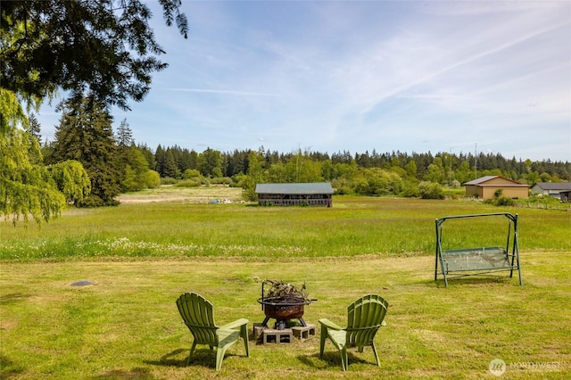 view of grassy yard with an outdoor fire pit and a wooded view