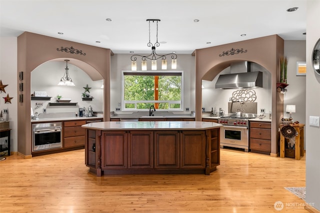 2720 NW Cascade Ave, East Wenatchee, WA 98802 - kitchen featuring appliances with stainless steel finishes, wall chimney range hood, a kitchen island, light countertops, and light wood-style flooring