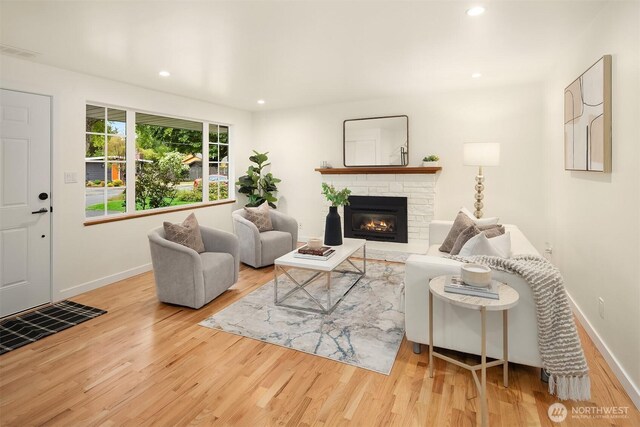 living area with wood finished floors, baseboards, a stone fireplace, and recessed lighting