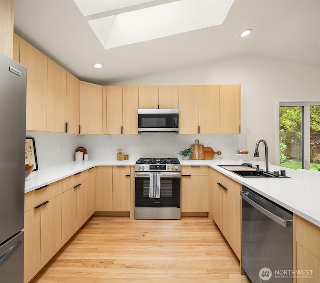 kitchen with appliances with stainless steel finishes, light brown cabinets, a skylight, a sink, and vaulted ceiling