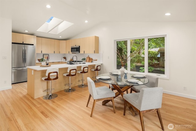kitchen with appliances with stainless steel finishes, a skylight, light brown cabinets, light countertops, and vaulted ceiling