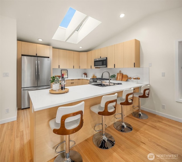 kitchen with appliances with stainless steel finishes, light brown cabinetry, a skylight, a peninsula, and vaulted ceiling