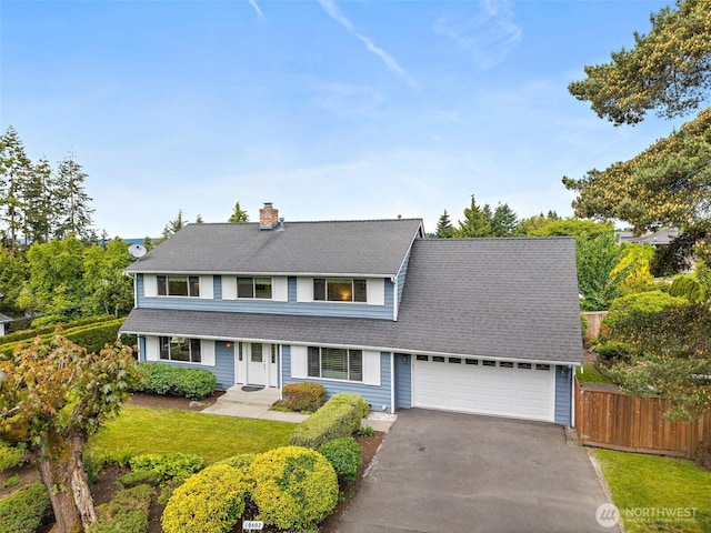 traditional-style house featuring fence, asphalt driveway, a garage, a chimney, and a shingled roof