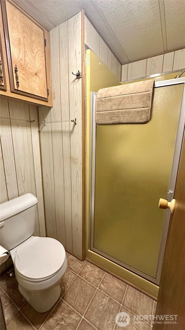 169 Twin Lakes Dr, Winthrop, WA 98862 - full bath with a stall shower, toilet, tile patterned flooring, wooden walls, and a textured ceiling