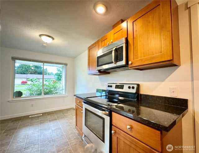 8312 121st St SW, Lakewood, WA 98498 - kitchen featuring appliances with stainless steel finishes, brown cabinets, baseboards, dark stone counters, and a textured ceiling