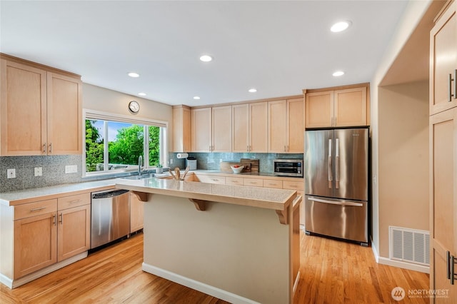 11120 NE 106th Pl, Kirkland, WA 98033 - kitchen featuring appliances with stainless steel finishes, light countertops, a kitchen breakfast bar, tasteful backsplash, and light wood-style flooring