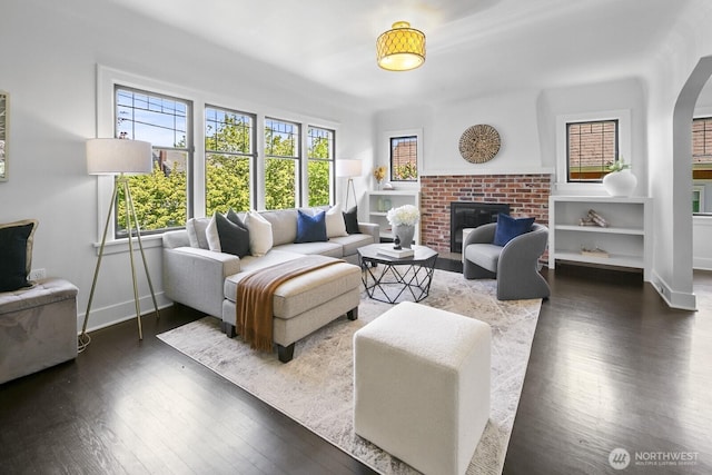 living room featuring wood finished floors, a brick fireplace, arched walkways, and baseboards