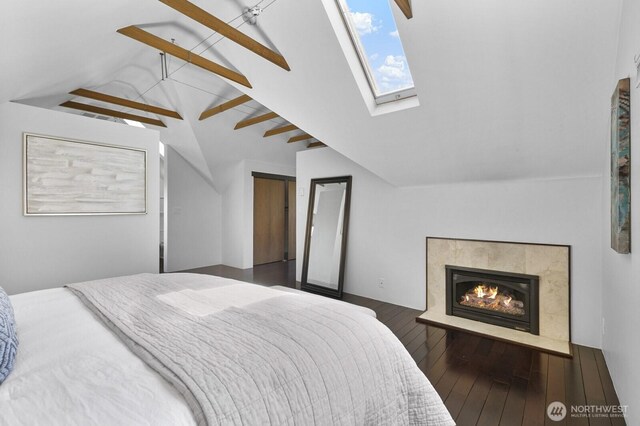 bedroom with lofted ceiling, a glass covered fireplace, wood finished floors, and a skylight
