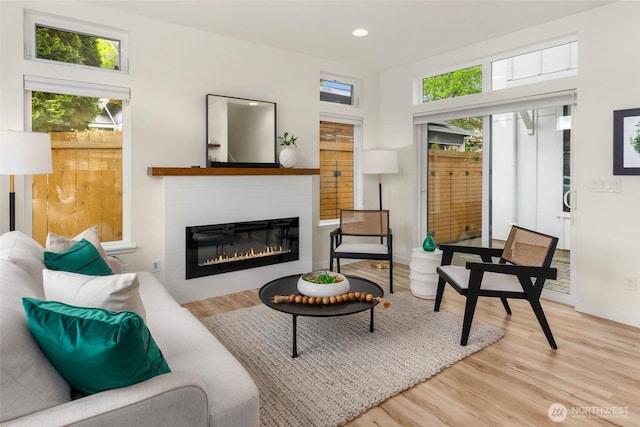 living area featuring plenty of natural light, wood finished floors, a glass covered fireplace, recessed lighting, and baseboards