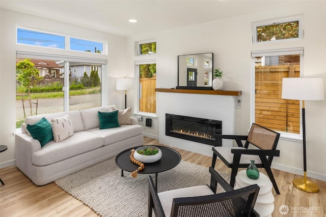 living area with a glass covered fireplace, light wood-style flooring, recessed lighting, and baseboards